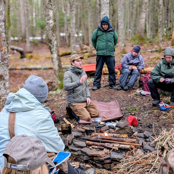 Group of people gathered around a campfire in a forest.