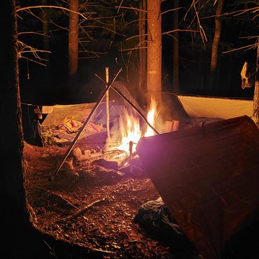 Campfire at night in a forest with a makeshift shelter.