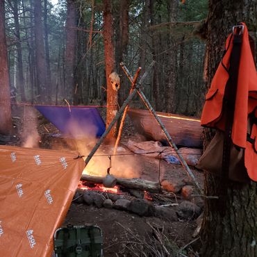 Cozy forest campsite with tarps and campfire.
