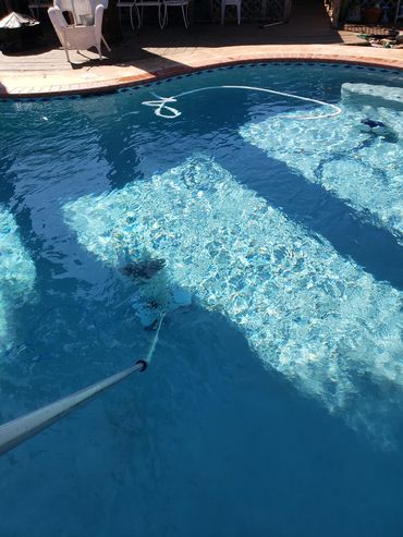 A pool being cleaned with a pole vacuum under sunlight.