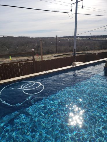 Sunlight sparkles on a clear backyard pool with a rural view beyond the wooden fence.