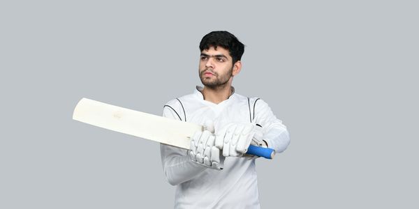 Cricket player in white gear holding a bat, ready to play.