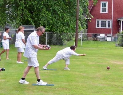 People playing lawn bowls on a grassy field near a red building.