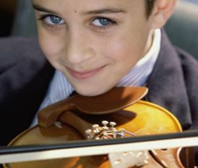 Smiling young boy with blue eyes playing a violin.