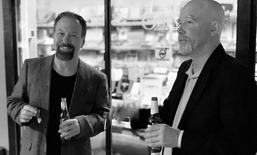Two men enjoying drinks and cigars, smiling.