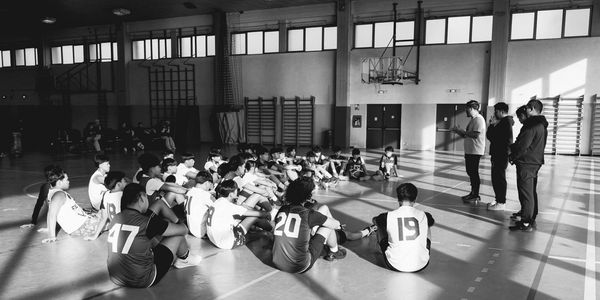 Youth basketball team sitting on gym floor listening to coaches.