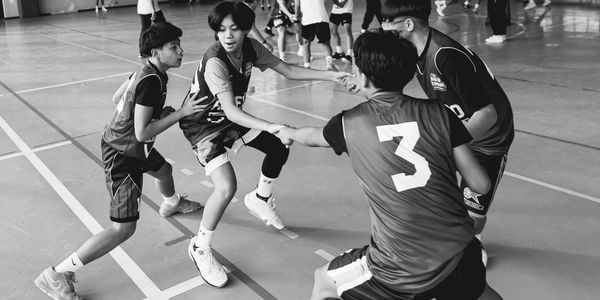 Youth basketball players holding hands in a circle on a gym court.