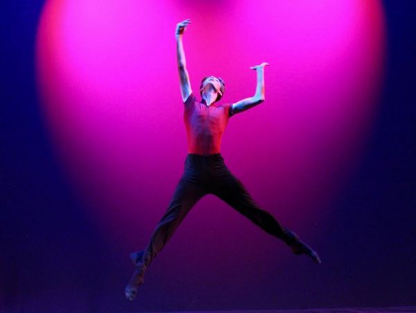 A dancer jumps gracefully in front of a pink heart-shaped light.