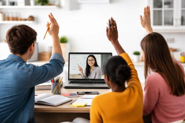Students raising hands during an online class with a teacher on laptop.