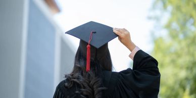 Graduate in cap and gown adjusting mortarboard.