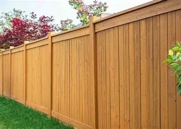 A tall wooden fence enclosing a garden area with green grass and flowering plants.