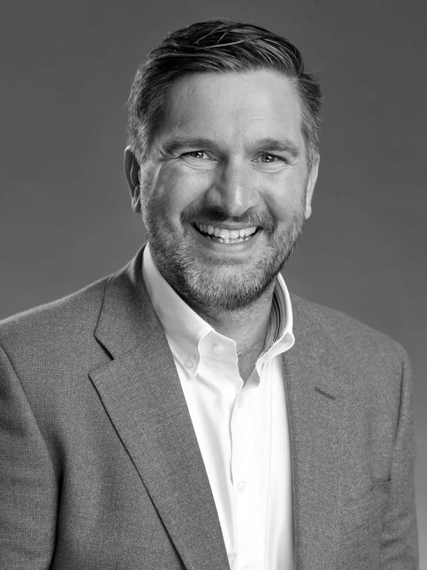 Smiling man in a blue blazer and white shirt against a neutral background.