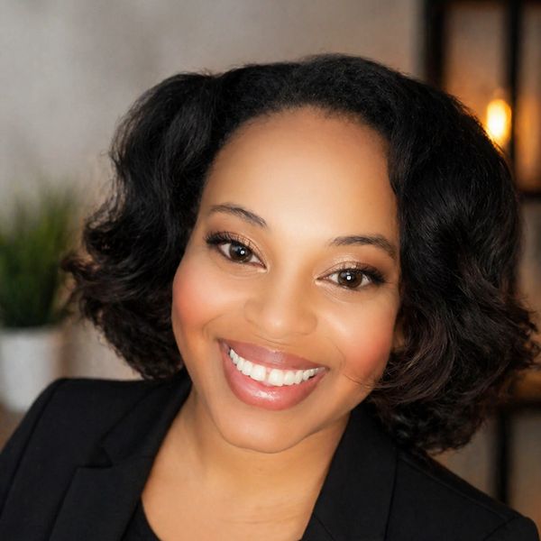 Smiling woman with natural curly hair wearing a black blazer.