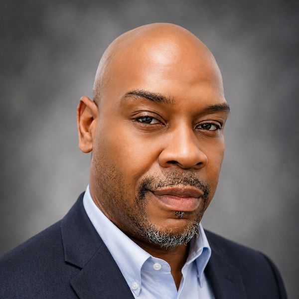 Confident man in a suit with a calm expression against a neutral background.