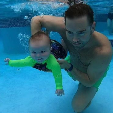 A man helping a baby swim in the swimming pool.