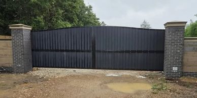 A large black metal gate between two brick pillars.