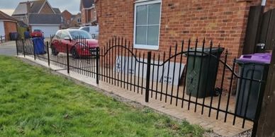 A black metal fence with uneven panels along a brick house.