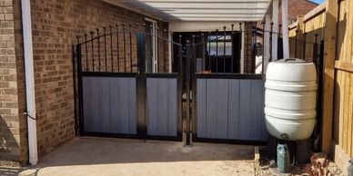A backyard gate with blue panels and a white rain barrel beside it.