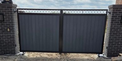 Modern black metal gate between brick pillars under a cloudy sky.