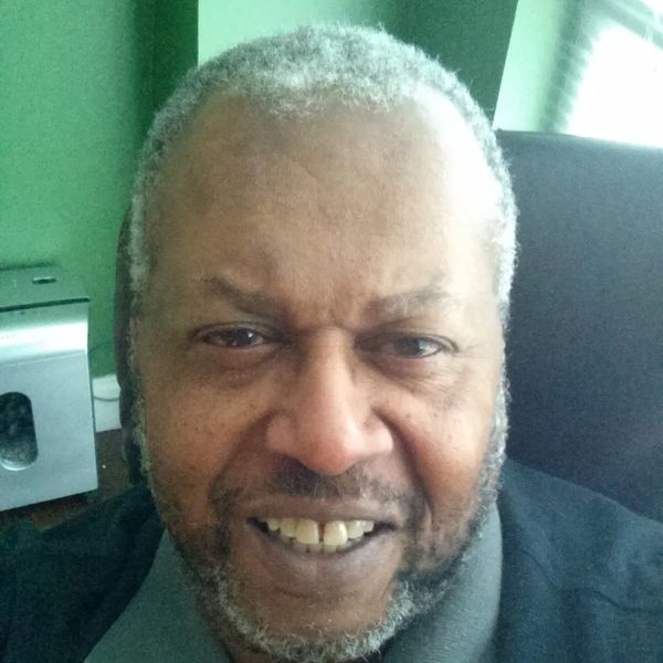 Close-up of a smiling man with gray hair and beard indoors.