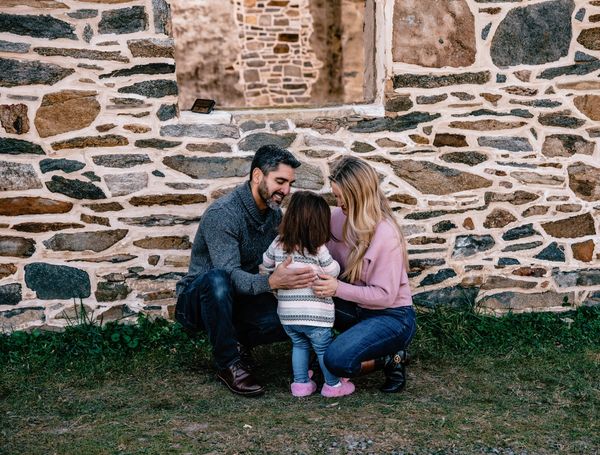 A family lovingly embraces their young child outdoors by a stone wall.