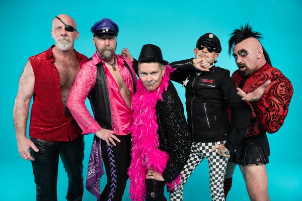 Five men in bold, eclectic costumes posing against a blue background.