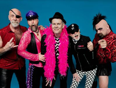 A colorful group of five men in eclectic, bold outfits posing against a blue background.