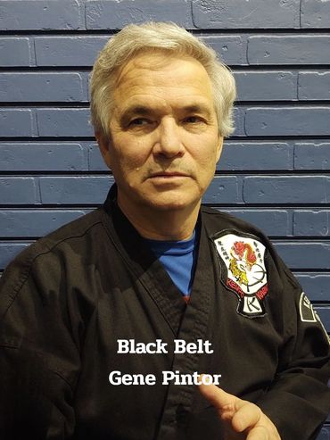 Martial artist Gene Pintor in black belt uniform posing against a blue brick wall.