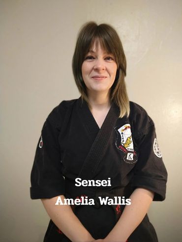 Sensei Amelia Wallis in a black martial arts gi with a calm smile.