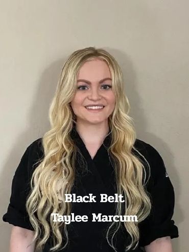 Smiling woman with long blonde hair wearing a black martial arts uniform.