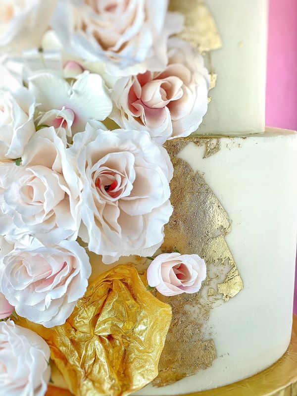 Extreme closeup photo of white wedding cake gilded with gold foil and covered in lush silk roses.