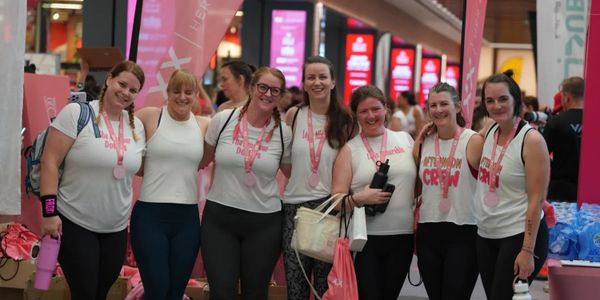 Group of women wearing matching shirts and medals, smiling together indoors.
