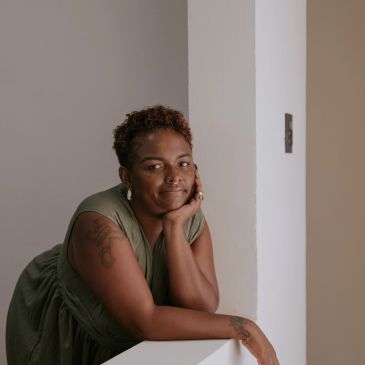 Woman with short curly hair leaning on a white surface.
