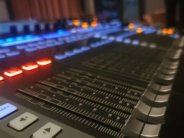 Close-up of an audio mixing console with illuminated buttons and sliders.