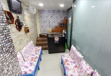 Cozy waiting area with floral sofas, stone accent wall, and a reception desk under a staircase.