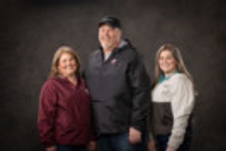 Three adults posing together against a dark background.