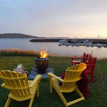 Four adirondack chairs around a fire pit overlooking the ocean from Legge’s Sunset Inn.