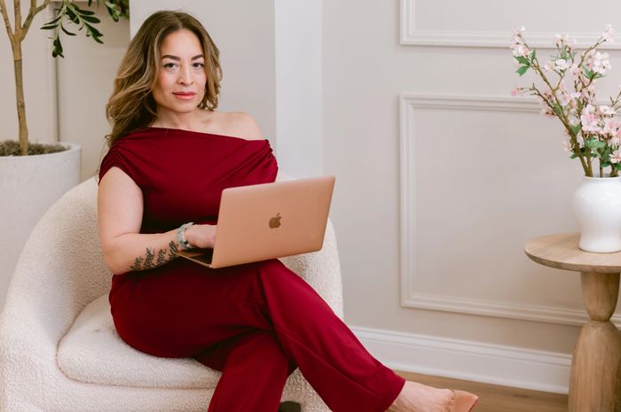 Woman in burgundy outfit sitting on chair with laptop on lap