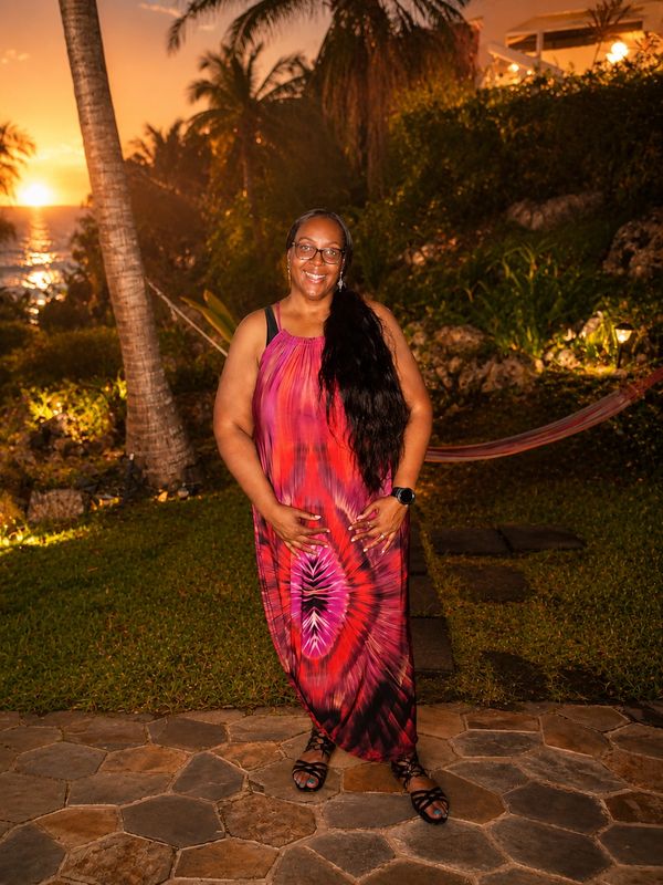 Woman smiling in a colorful dress at sunset near palm trees.