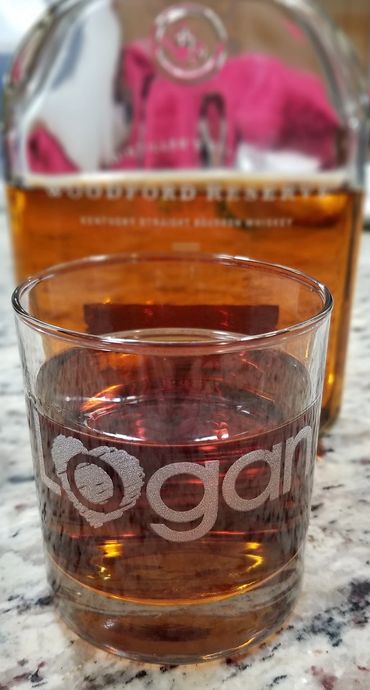 Clear whiskey glass etched with "Logan". Whiskey decanter in background.