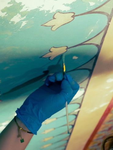 Une main gantée peint un mur turquoise avec des fleurs.