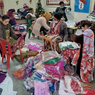 People sorting and packing colorful clothes indoors, around a Christmas tree.