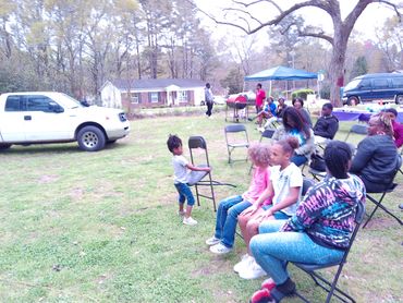 A group of people gathered outdoors with children and adults sitting and standing.