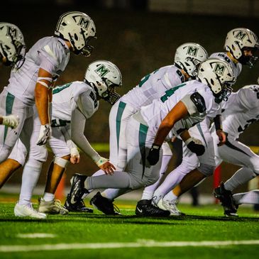 Football players in white uniforms lined up on the field ready to sprint.
