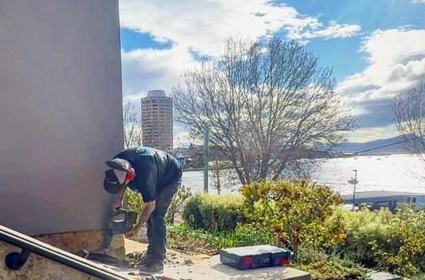 A person working outdoors with a power tool near a building on a sunny day.