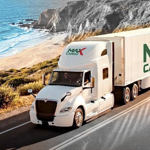 Camión blanco Max Cargo en carretera costera.