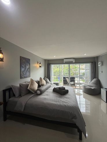 Modern bedroom with gray tones, a large bed, and a balcony with outdoor seating.