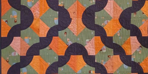 Quilt with orange, green, and dark purple geometric patterns.