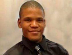 Young man in a black shirt and tie smiling.