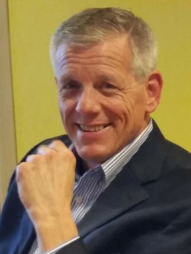 Smiling man in a suit jacket posing with a fist near his chin.